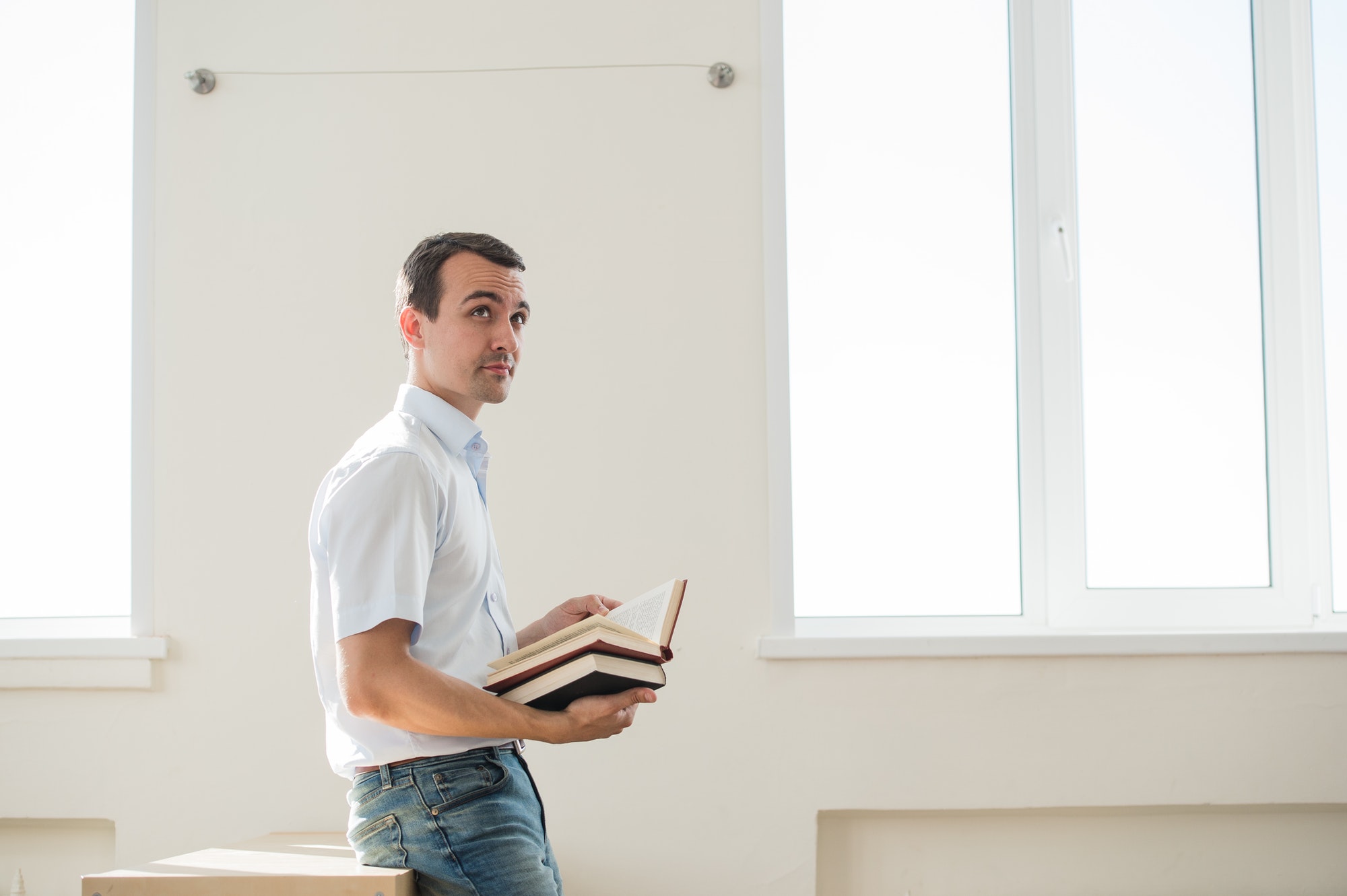 Thoughtful handsome pensive young man studying at class or living room, reading a book