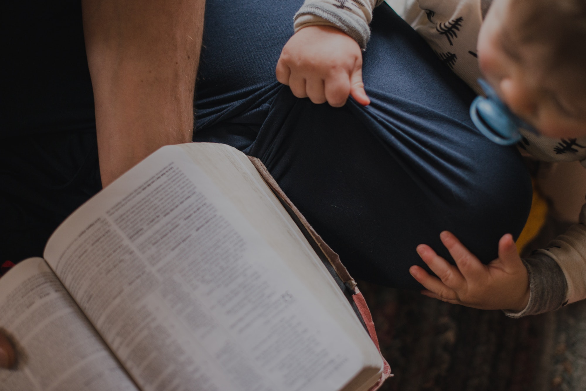 Little boy on his father's knee while his dad reads Scripture