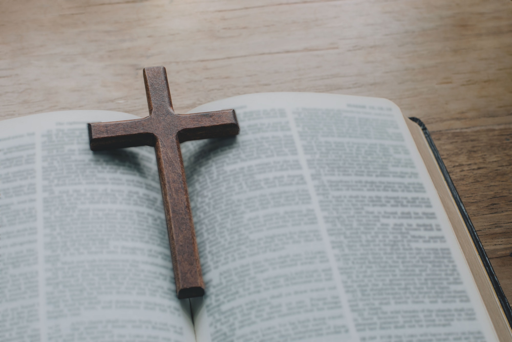 Closeup of simple wooden Christian cross necklace on Bible.